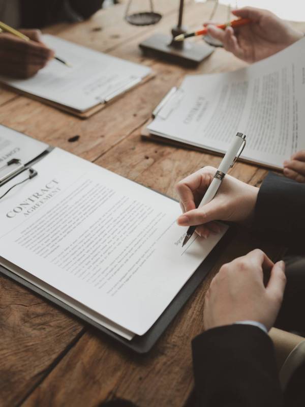Business people negotiating a contract, discussing contract while working together in sunny modern office, unknown businessman and woman with colleagues or lawyers at meeting.
