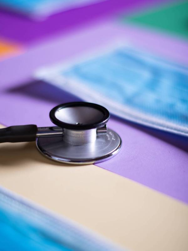 A vertical shot of a stethoscope on colorful papers with facemasks on the table - COVID-19